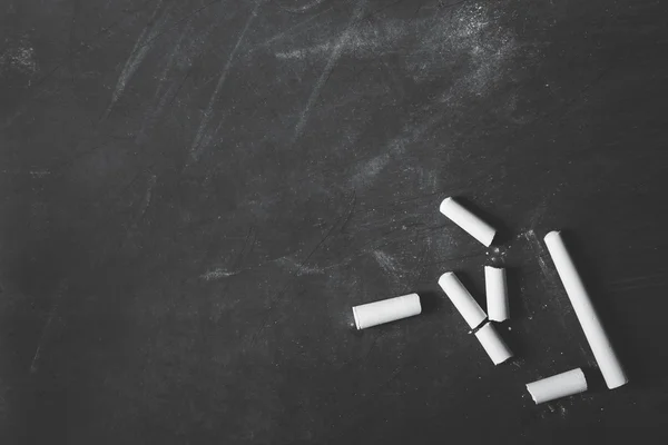 Some white chalks on blank black board — Stock Photo, Image