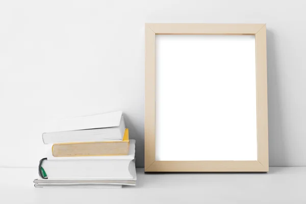 Desk blank photo frame nest to stack of books — Stock Photo, Image