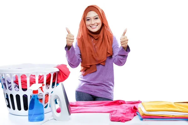 Young woman wearing hijab ironing clothes and giving two thumbs — ストック写真
