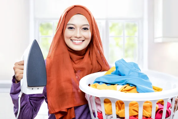 Joven sonriente mujer usando hijab sosteniendo hierro y llevando laun —  Fotos de Stock