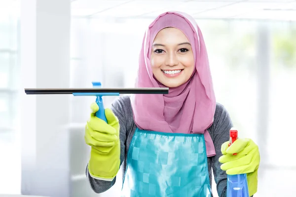 Wanita muda membersihkan jendela dengan squeegee dan semprotan pembersih — Stok Foto