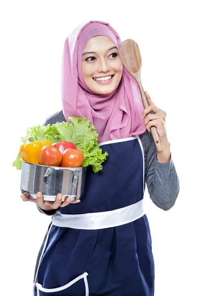 Mujer joven llevando una sartén llena de verduras y espátula de madera — Foto de Stock