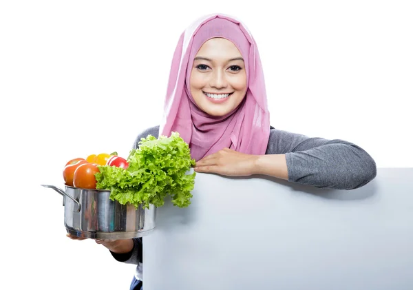 Jovem mulher sorridente carregando uma panela cheia de legumes com as mãos — Fotografia de Stock
