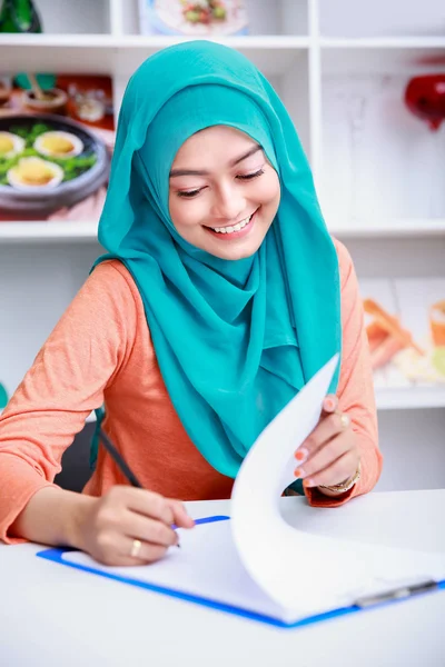 Smuk muslimsk kvinde skriver på papir - Stock-foto