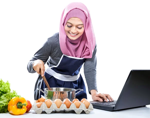 Mujer joven usando hijab cocinar con referencia a la computadora portátil —  Fotos de Stock