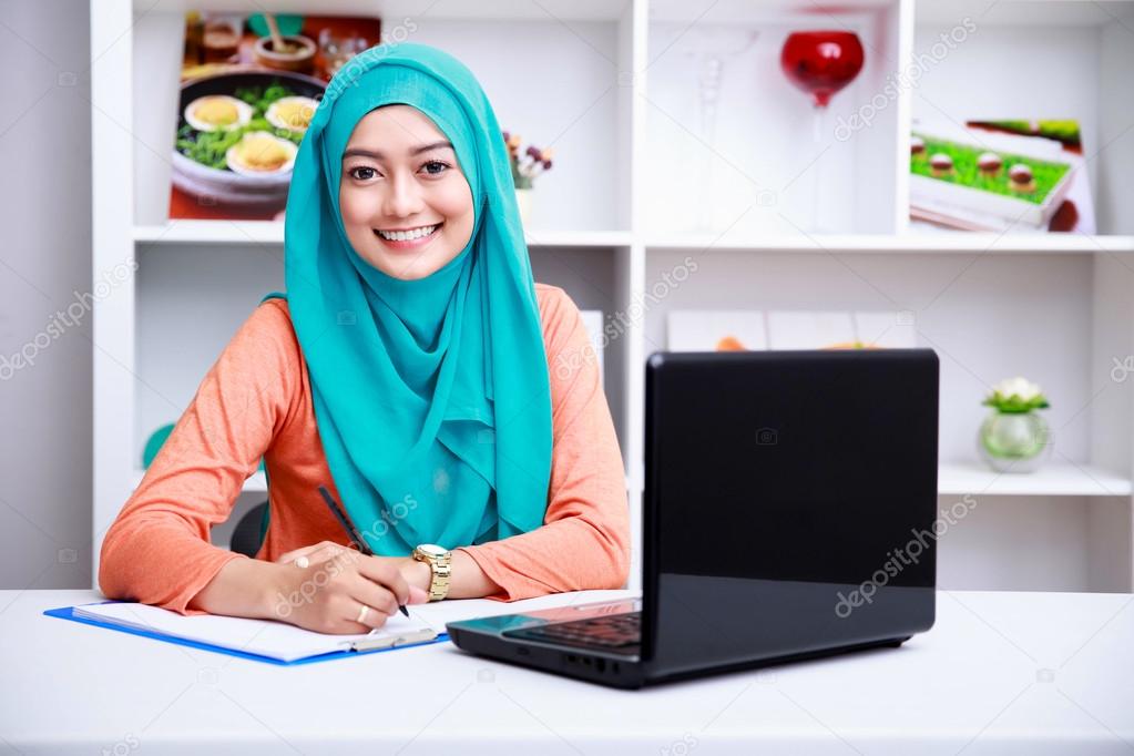 beautiful muslim woman writing an information from laptop