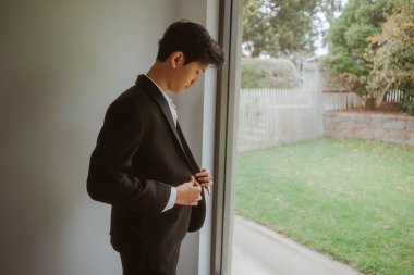 Şık bir genç adam yaklaşan bir etkinlik için elbisesini büyük bir pencerenin yanında ayarlar.