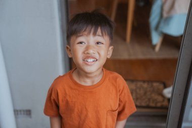 Sıcak bir gülümsemesi olan neşeli bir çocuk kapıda duruyor, saf neşe saçıyor.