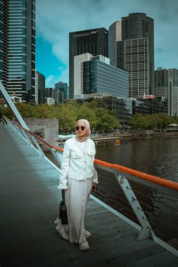 Şık bir kadın gündüzleri hareketli bir şehirde modern bir köprüde geziniyor.