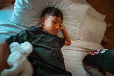 Genç bir çocuk yatağında yatıyor, rüyalarını ve çocukluk maceralarını yansıtıyor.