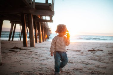 Gün batımında plajı keşfeden çocuk, kumlu sahil şeridinde yalın ayak yürüyen genç çocuk.