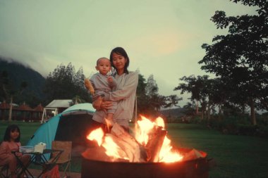 Huzurlu ve huzurlu bir aile kamp sahnesi alacakaranlıkta sıcak bir ateşin altında toplanan çocuklarla gözler önüne seriliyor.
