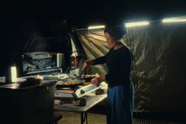 Bir kampçı gece lezzetli bir yemek hazırlıyor. Vahşi doğadaki yumuşak ışıklarla güzelce aydınlatılıyor.