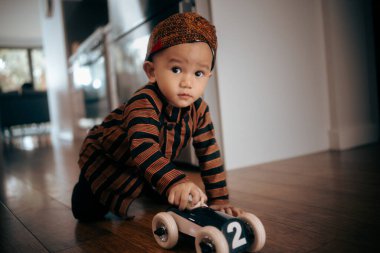 Neşeli genç bir çocuk şık bir evde oyuncak bir arabayla oynuyordu.