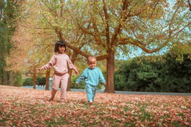 Çocuklar sonbahar yapraklarını keşfediyor, iki çocuk solgun yaprakların arasında geziniyor.
