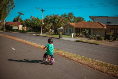 Çocuk, sıcak güneş ışığı altında sakin bir mahallede neşeyle süzülüyor.