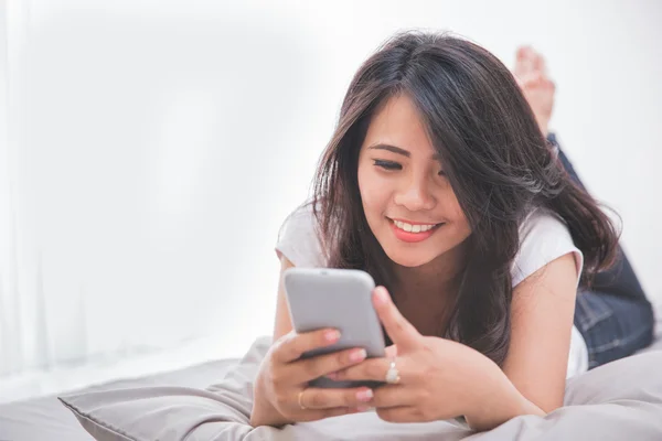 Vrouw met behulp van mobiele telefoon op het bed — Stockfoto