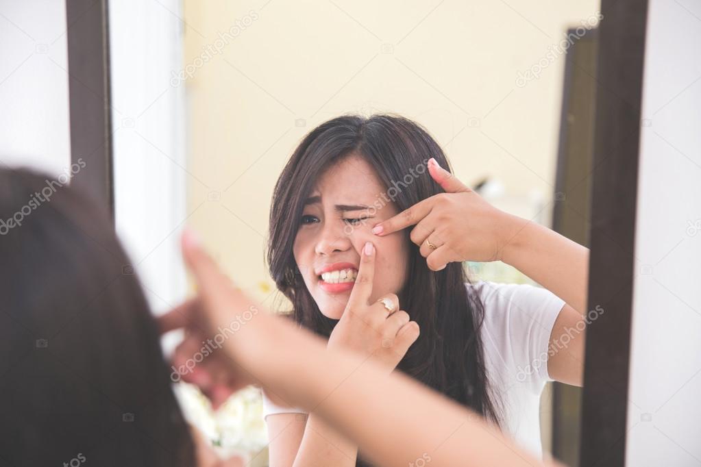 Woman squeezing pimples look at the mirror