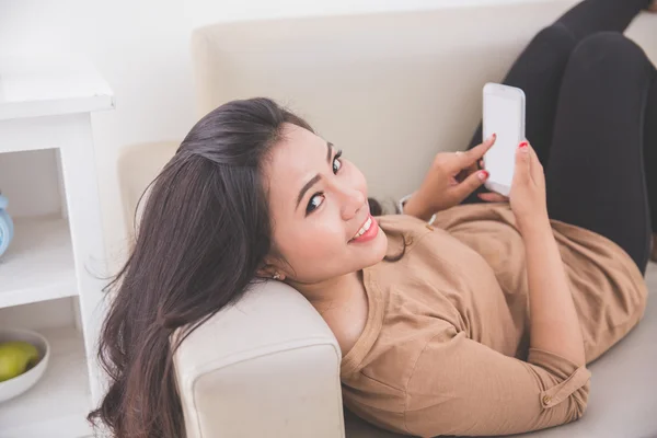 Donna sdraiata su un divano e con un cellulare in mano — Foto Stock