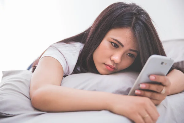 Frau benutzt Handy auf dem Bett — Stockfoto