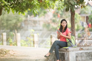 Açık otururken, bir cep telefonu tutan genç Asyalı öğrenci