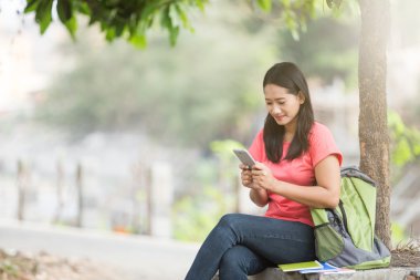 Açık otururken, bir cep telefonu tutan genç Asyalı öğrenci