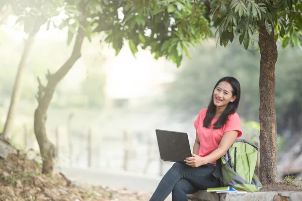 Ung asiatisk student sitter utomhus, använder en bärbar dator — Stockfoto