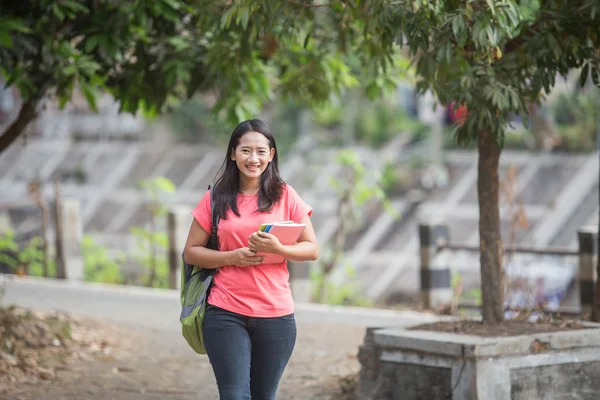 Mahasiswa muda Asia berjalan di luar ruangan sambil memegang bukunya — Stok Foto