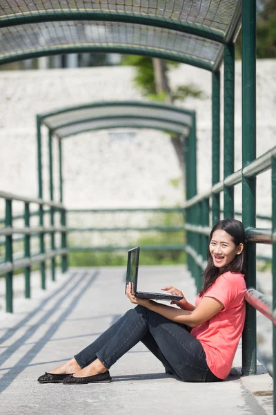 Genç Asyalı öğrenci açık otururken, bir dizüstü bilgisayar kullanarak — Stok fotoğraf