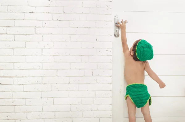 Μικρό παιδί με πράσινο καπέλο και παντελόνι, προσπαθώντας να φτάσει τη λαβή της πόρτας — Φωτογραφία Αρχείου