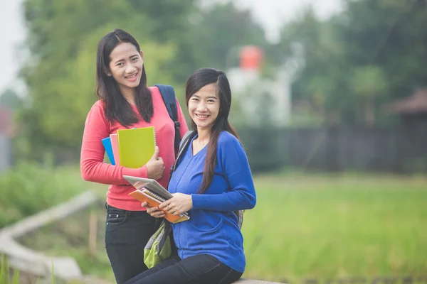 Två unga asiatiska studenter hålla böcker, leende ljust till den — Stockfoto