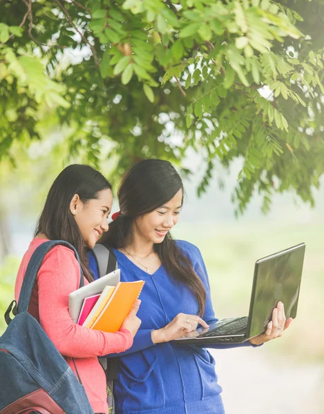 Two young Asian students standing together, one holding a laptop — Stock Photo, Image