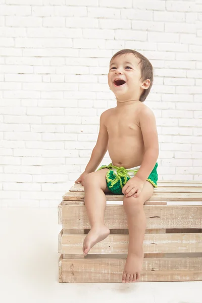 Cute handsome toddler laughing while sitting on wooden box — Stock Photo, Image