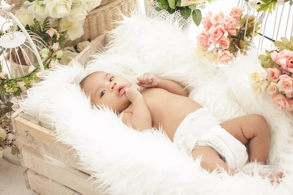 Pretty baby girl in box with fur blanket and flowers around — Stock Photo, Image