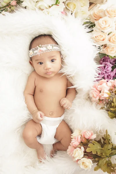 Adorável bebê menina deitada em manta de pele com flores ao redor — Fotografia de Stock