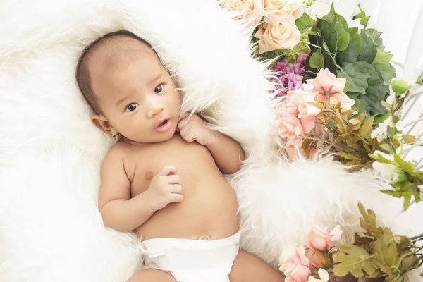 Schattige babymeisje liggend op bont deken met bloemen rond — Stockfoto