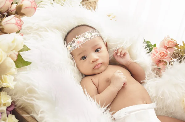 Bonito bebê menina deitado no cobertor de pele com flores ao redor — Fotografia de Stock