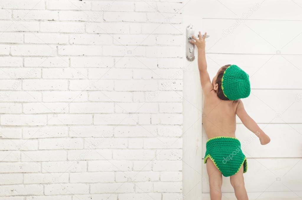 toddler with green hat and pants trying to reach door handle