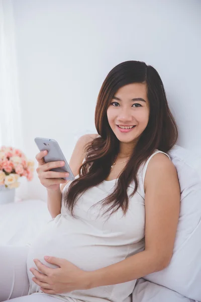 Zwangere Aziatische vrouw met behulp van een smartphone — Stockfoto
