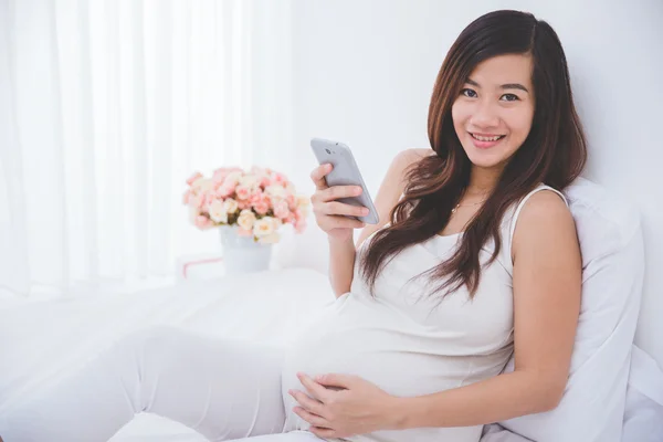Беременная азиатка с помощью смартфона — стоковое фото