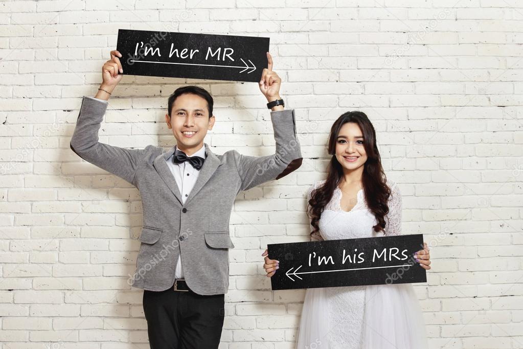 handsome groom and beautiful bride smiling while holding board