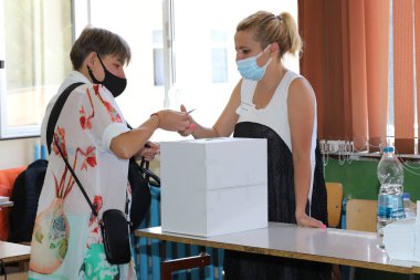 Maskeli insanlar 11 Temmuz 2021 'de Bulgaristan' ın Sofya kentinde yapılan parlamento seçimlerinde oy kullanma makinesi kullanıyorlar