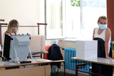 Maskeli insanlar 11 Temmuz 2021 'de Bulgaristan' ın Sofya kentinde yapılan parlamento seçimlerinde oy kullanma makinesi kullanıyorlar