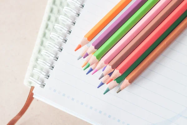 Top view of colorful pencil crayons on spiral notebook and green — Stock Photo, Image