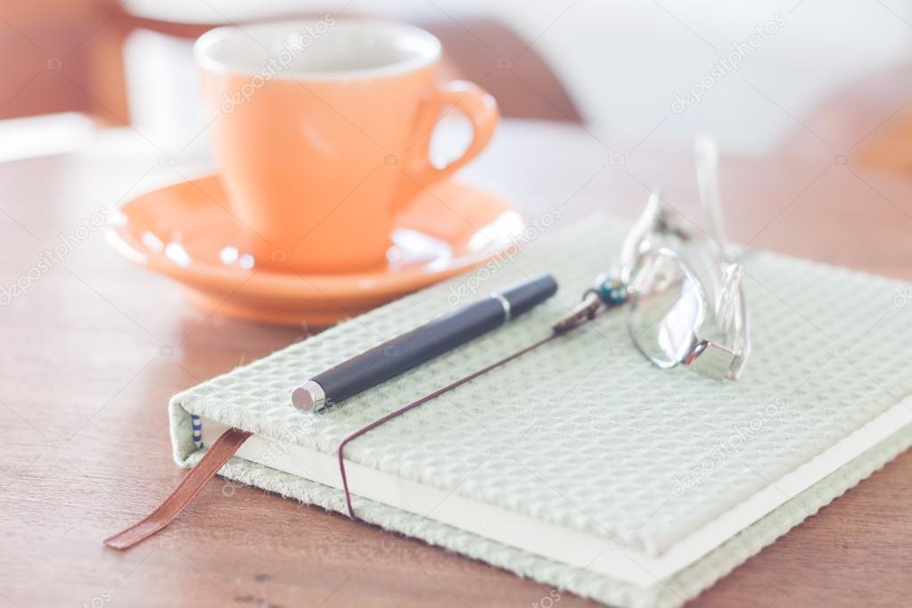 Notebook, pen and eyeglasses with orange coffee cup