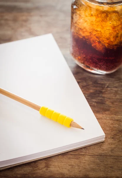 Pencil on open blank notebook with glass of iced cola — Stock Photo, Image