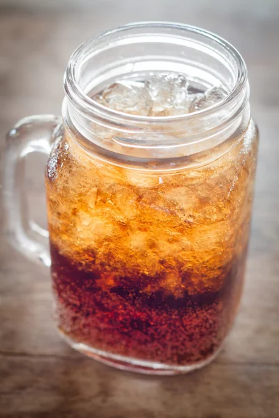 Sklenice cola s ledem na dřevěný stůl — Stock fotografie