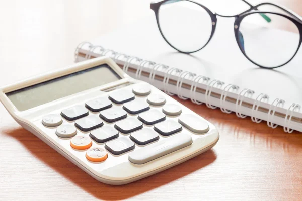 Calculator with eyeglasses on wooden table — Stock Photo, Image