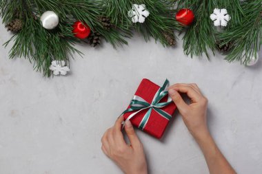 Yeni yıl hediyesini paketleyen bir kadın kurdele bağlar. Gri arka plan. Yılbaşı kartı. Boks günü. Üst görünüm
