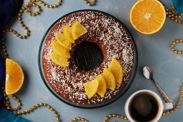 Ortasında delik olan portakallı ev yapımı kek, açık mavi bir arka plan ve bir fincan kahve üzerine hindistan cevizi taneleri serpiştirilmiş. Yukarıdan görüntüle